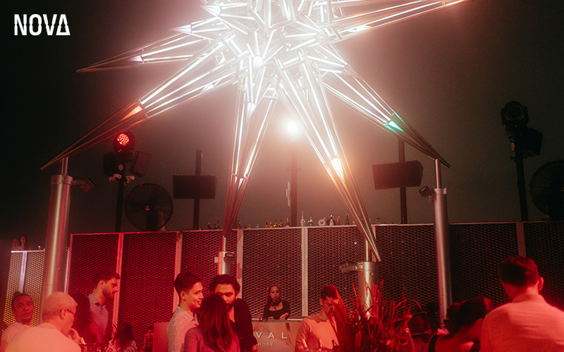 People socializing under a lighted sculpture on a rooftop bar.